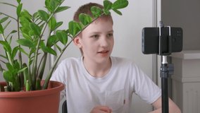 Boy blogger in yellow headphones greets followers. Teenager live streaming looking to smartphone screen and gestures at home