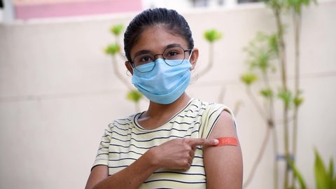 Portrait of an Indian teen getting vaccinated and showing bandage on his arm. with wearing protective mask