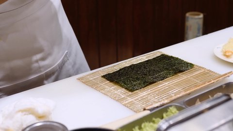 Japanese Chef working make traditional delicious Japanese food "Maki roll sushi", place deep fried shrimp tempura on rice, seaweed roll with bamboo on sushi bar counter. 