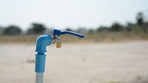 Water shortage concept.Close up tied Asian boy open metal blue water faucet on hot and dry empty land. 