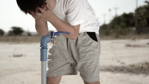 Water shortage concept.Close up tied Asian boy open metal blue water faucet on hot and dry empty land. 