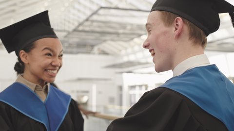 Rear view of young mixed-race female graduate hugging her male Caucasian friend wearing university graduate gowns and caps during graduation day