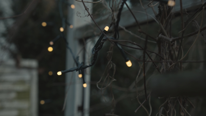 Shot of warm white outdoor fairy lights illuminated, draped over a window, shot in the evening light.