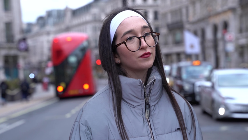 Cute girl flirting with camera standing in streets of London. Smiling shyly.
