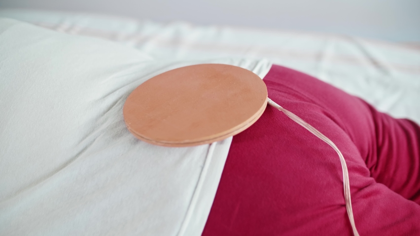 Close up view of woman lying face down on bed with special coil on her rump. Alternative medecine.