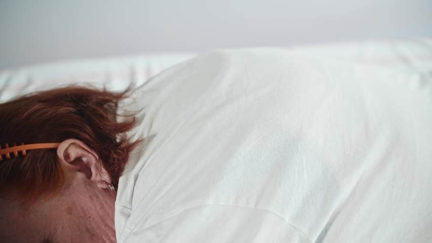 Woman lies face down on bed and hand puts special coil on upper part of her back. Alternative medecine. Side view.