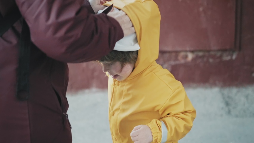 Mom puts on a little girl hood in a strong wind. The hurricane overtook the family suddenly and the child is confused. The concept of the elements and the storm