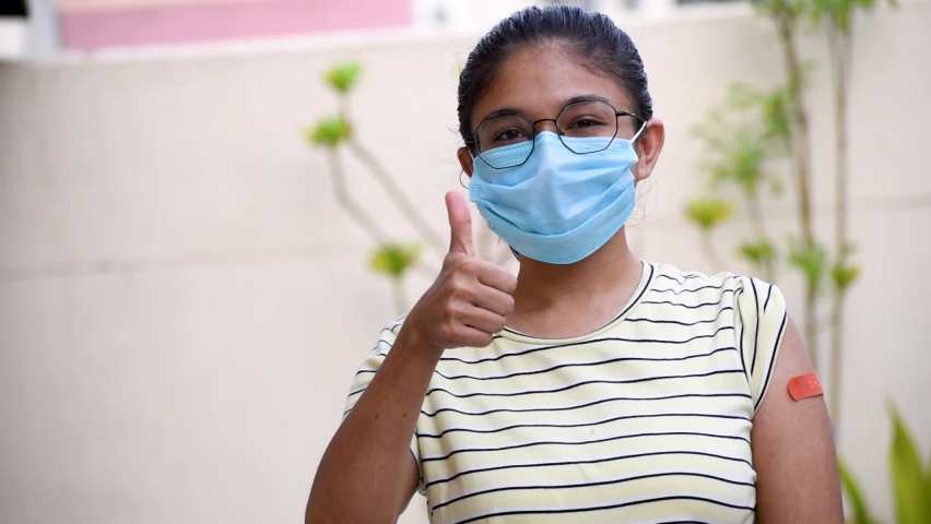 Portrait of an Indian teen giving thumbs up after getting vaccinated and showing bandage on his arm. with wearing protective mask | Shutterstock HD Video #1072668356