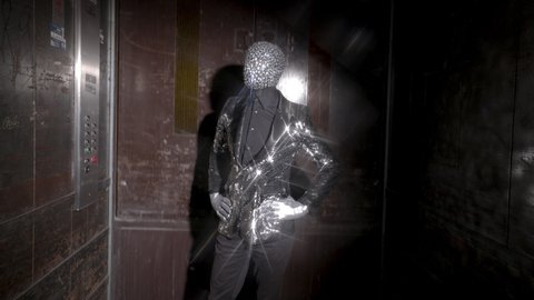 A man with a sparkling mask over his face enters an industrial elevator 