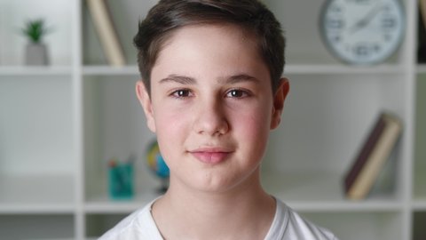 Portrait of happy boy of 12-13 years old in white shirt looking at camera and smiling at home. Handsome teenager schoolboy, close-up