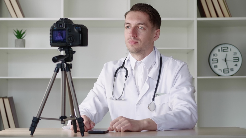 Doctor videoblogger records a video blog for the Internet, a medical man consults on the Internet on the camera, sitting at the table in the office of the clinic Royalty-Free Stock Footage #1072673540