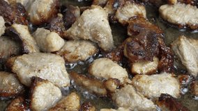 4K video clip of frying pieces of meat in a frying pan with oil at high temperature close-up.