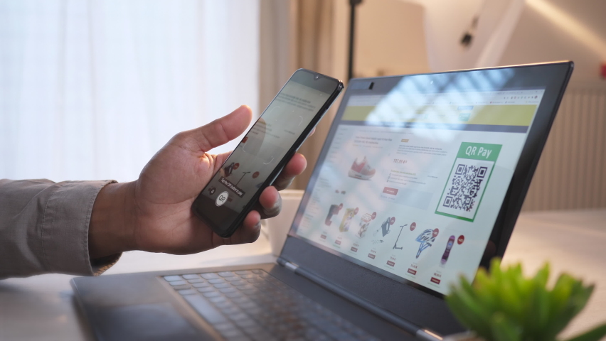 Handheld shot of an African-American male hand holding a mobile phone, using together with a laptop for online shopping, scanning QR code and paying with bitcoins via the mobile app Royalty-Free Stock Footage #1072686044