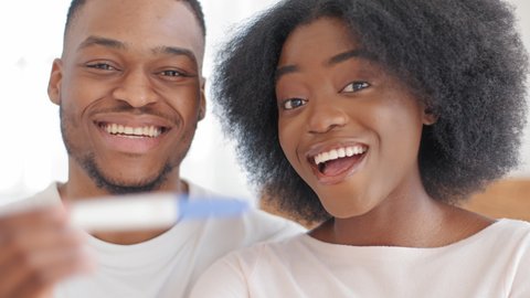 Portrait of happy african american couple married newlyweds afro man husband and curly beautiful pregnant woman future parents show positive pregnancy test smiling rejoice expecting unborn baby child 