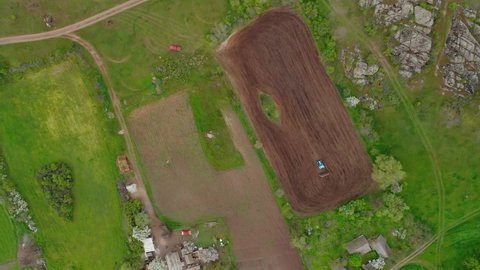 Aerial view of a tractor planting a field on a small plot of fertile land. Heavy machinery when sowing, working in the fields. Aerial view of a tractor sowing land in a field.