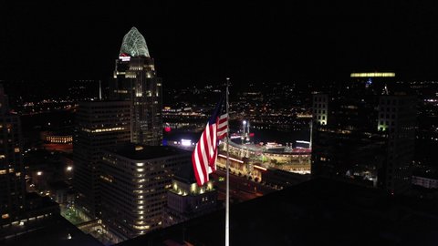 Cincinnati, Ohio, USA - May 18 2021: 4K Drone aerial footage of downtown Cincinnati, Ohio. Circling an American flag waving in the wind at the top of a skyscraper at night.