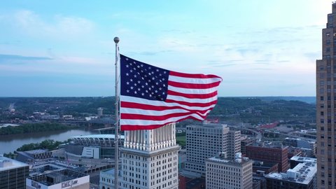Cincinnati, Ohio, USA - May 18 2021: 4K Drone aerial footage of downtown Cincinnati, Ohio. Circling an American flag waving in the wind at the top of a skyscraper. Arcing reveals Carew Tower and PNC.