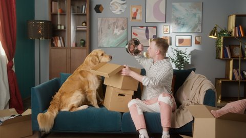 Man carrying and opening online delivery box with his retriever dog, e-commerce shopping for pets, food and toys gift for small animal friends, british student and his puppy at home. 