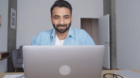 Young happy indian male teacher talking on webinar video training using pc laptop at modern home office. Hispanic businessman on interview, talking to team online. Remote distant online work concept.