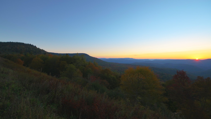 Panning West Virginia Monongahela national forest overlook with woman photographer taking photos of colorful autumn mountains at morning sunrise near Highland Scenic Highway