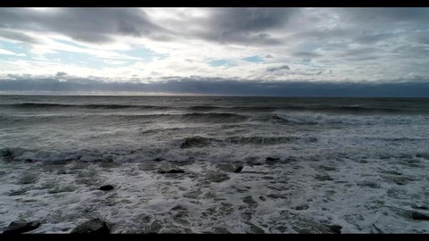 Rough ocean waves crashing into rocky beach shore on cloudy day