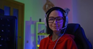 Portrait of a beautiful woman gamer getting ready to play the cyber game online. Streamer gamer sits in headphones with a headset and smiles, the player is the winner. 4k, ProRes