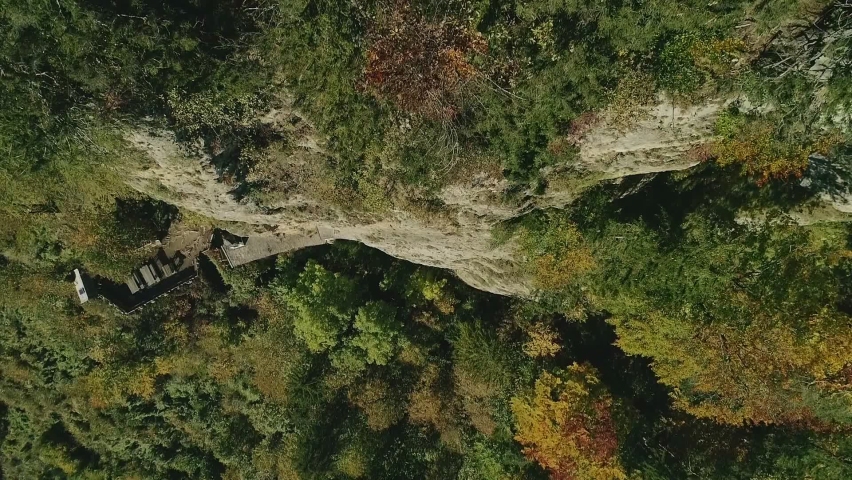An aerial drone shot flying over the edge of a rocky cliff looking straight down. Daytime.