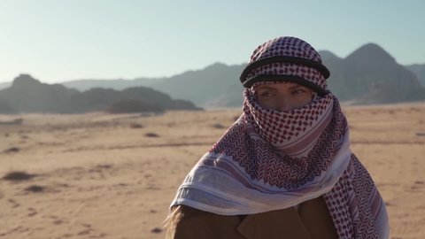 Amazing Slow motion close-up of a beautiful white woman tourist with green eyes dressed as a local Bedouin wearing a keffiyeh walking in the desert of Wadi Rum in Jordan on a beautiful clear sunny day