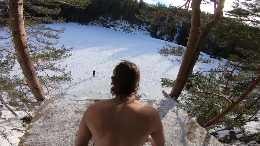 Thrill seeker does a death dive from a cliff into a hole cut into the ice far below - over the shoulder slow motion