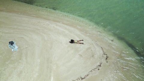 Aerial view of a sexy girl in a thong bikini laying in the sand on a sandbar in the crystal clear waters of the tropical island of Tobago