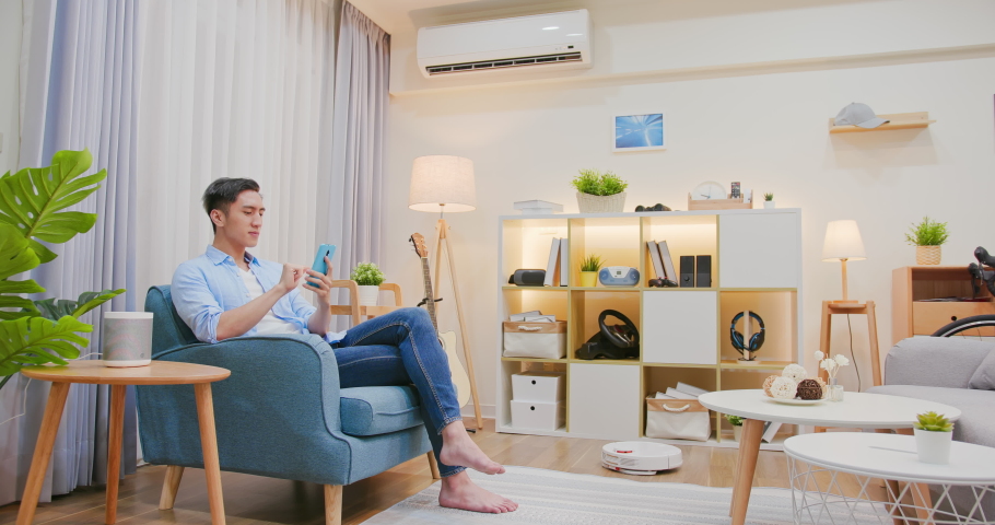 Asian man sitting on sofa and using smart home control app on mobile phone with augmented reality view of IOT connected objects in apartment | Shutterstock HD Video #1072706579