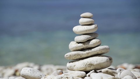 Stone balance closeup. Female hand making pebbles tower from sea stones. Macro of pyramid of pebbles on beach.