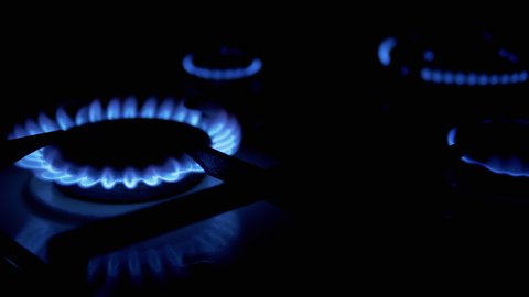 Four Gas burners on, glowing with blue flame, at night in the kitchen. Close-up. Gas stove on black background. A dangerous method of heating room. Natural gas is burning. 4K.
