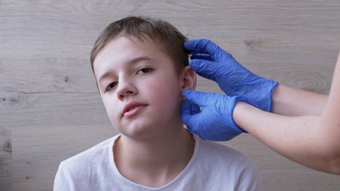 Doctor, ENT in Latex Nitrile Gloves Examines the ears, Auricle of a Teenage Boy. An otolaryngologist examines a young patient complaining of pain. A child at a doctor appointment. 4K. Close up.