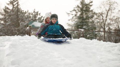 Happy children tobogganing down a snowy hill, slow motion.