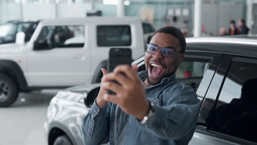 Joyful black guy takes a selfie in a car dealership Royalty-Free Stock Footage #1072717283