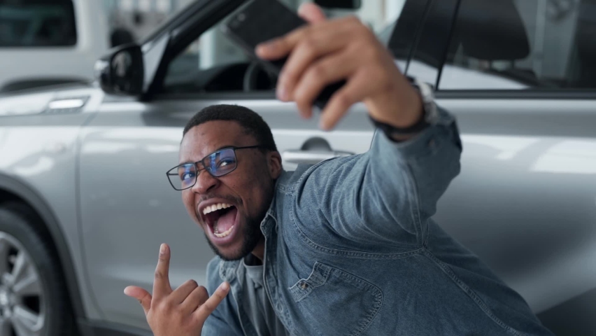 A black man happily shoots a video near the car in a car dealership Royalty-Free Stock Footage #1072717700
