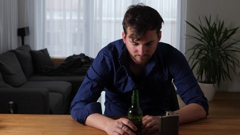 Medium shot of a young hangover man drinking beer at home in modern apartment.
