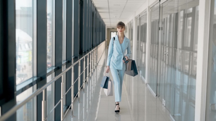 Stylish young girl with packages walks down the glass corridor and smiles