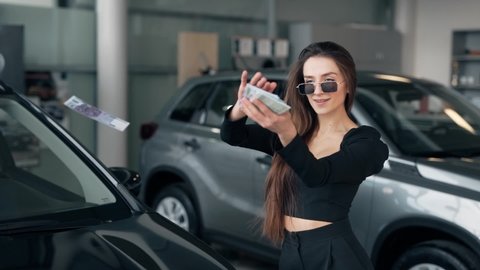 Happy smiling attractive girl scattering banknotes money on the car