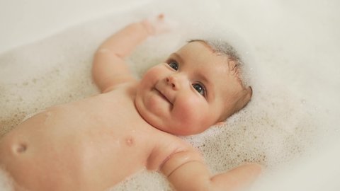 side view portrait of a little girl lying on her back in a large bath with foam