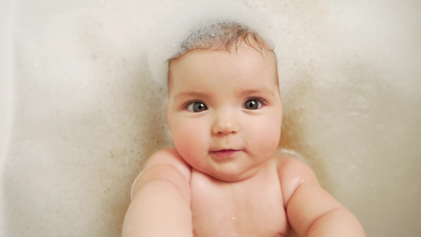 Close-up of a little baby girl lying on her back in the bathroom all in foam | Shutterstock HD Video #1072718867