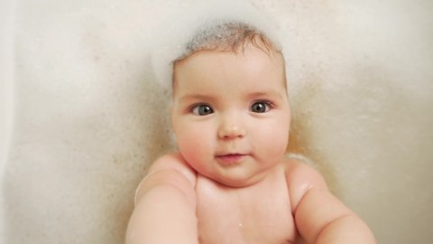 close-up of a little baby girl lying on her back in the bathroom all in foam