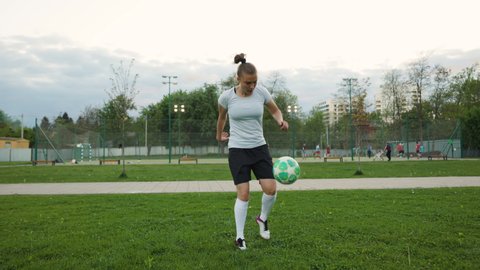 Portrait of woman football soccer player in full growth in the park. Woman in professional uniform juggling with ball. Men play football background