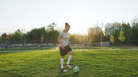 Portrait of woman football soccer player in full growth in the park. Woman in professional uniform juggling with ball. sunset background