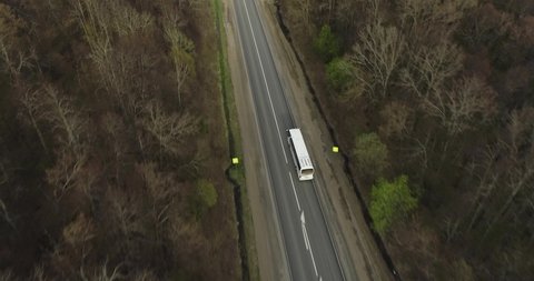 Travel tour bus driving on russian 
highway through dense skin forest. White bus fast speed moving on freeway. Aerial drone wide shot at spring sunset