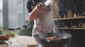 Midsection shot of male chef in apron adding chopped parsley to meat and tossing food on hot skillet while cooking meal in kitchen - Powered by Shutterstock - Get 15% off with code: PIKWIZARD15