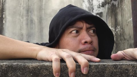 Asian man wearing a shirt with a black hood climb up concrete walls appearing suspiciously