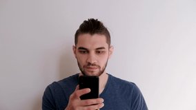 Young Caucasian man with beard and stylish hairstyle in blue Tshirt on white background is talking on phone, angry and waving his hands. Man throws smartphone aside after unpleasant conversation.