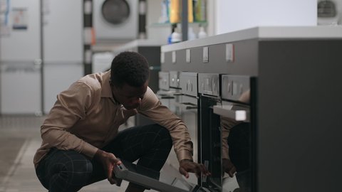 afro-american man is shopping in home appliances store, black guy is choosing equipment for home kitchen